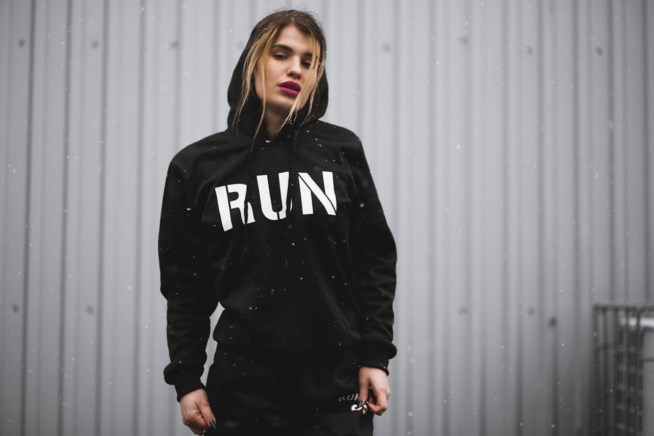 A woman in a black 'RUN' hoodie poses in an urban setting, exuding fashion and confidence.