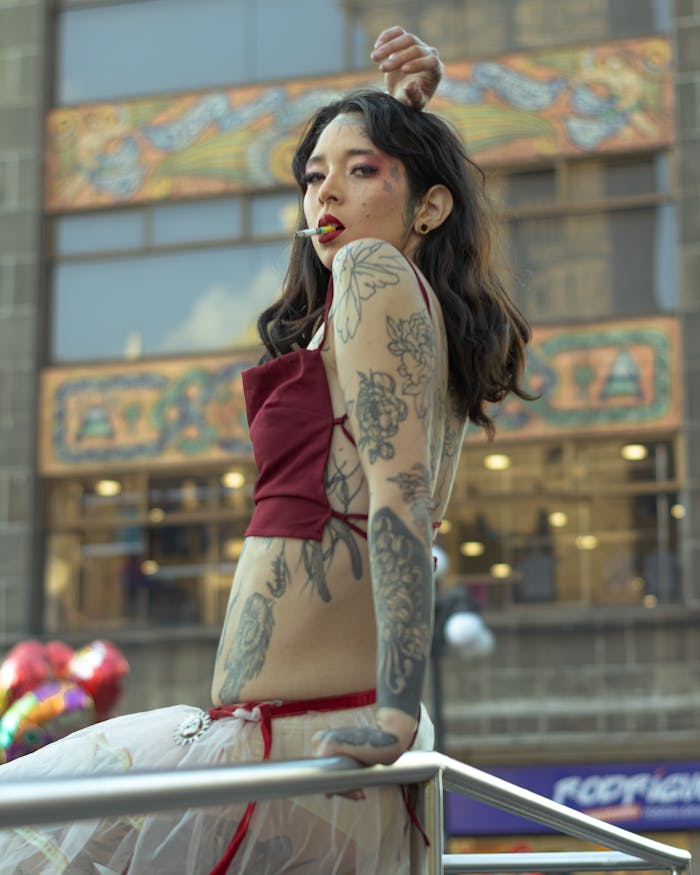 Fashionable woman with tattoos poses in an urban setting, surrounded by balloons.